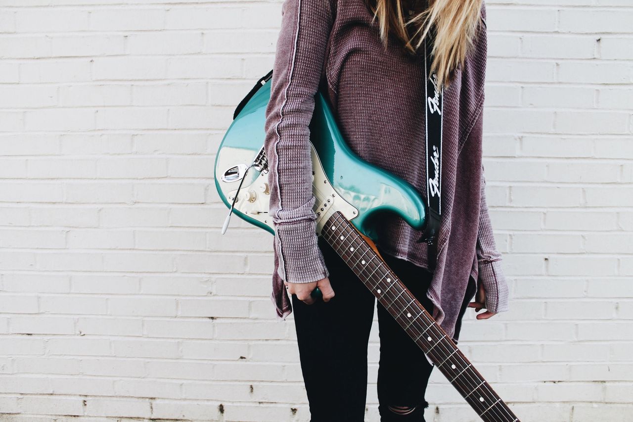 woman holding electric guitar - electric vs. acoustic guitar